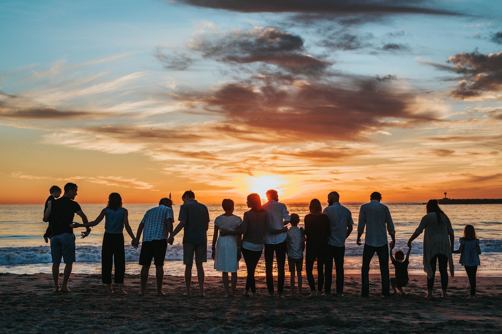 Família de várias gerações de mãos dadas diante do pôr do sol